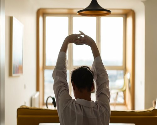 A person stretching gently by the window during a work break